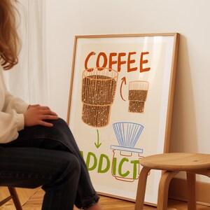 Pu&ograve; includere: Un poster incorniciato con un'illustrazione disegnata a mano di una tazza di caff&egrave; e il testo "COFFEE ADDICT". Il poster ha uno sfondo beige chiaro con accenti marroni, arancioni e blu.
