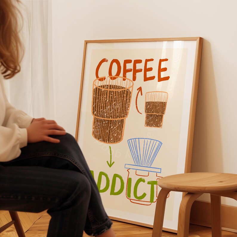 Pu&ograve; includere: Un poster incorniciato con un'illustrazione disegnata a mano di una tazza di caff&egrave; e il testo "COFFEE ADDICT". Il poster ha uno sfondo beige chiaro con accenti marroni, arancioni e blu.