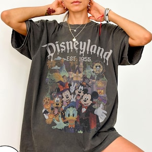Puede incluir: Una camiseta de manga corta gris carb&oacute;n con un estampado gr&aacute;fico de personajes de Disney con disfraces de Halloween. El texto dice Disneyland EST. 1955. El dise&ntilde;o incluye a Mickey Mouse, Minnie Mouse, Donald Duck y Pluto en un castillo.