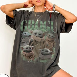 Puede incluir: Camiseta gris oscuro con la palabra "GROGU" en letras verdes en bloque sobre un gr&aacute;fico de Grogu, tambi&eacute;n conocido como Baby Yoda, de The Mandalorian. El gr&aacute;fico muestra a Grogu en varias poses.