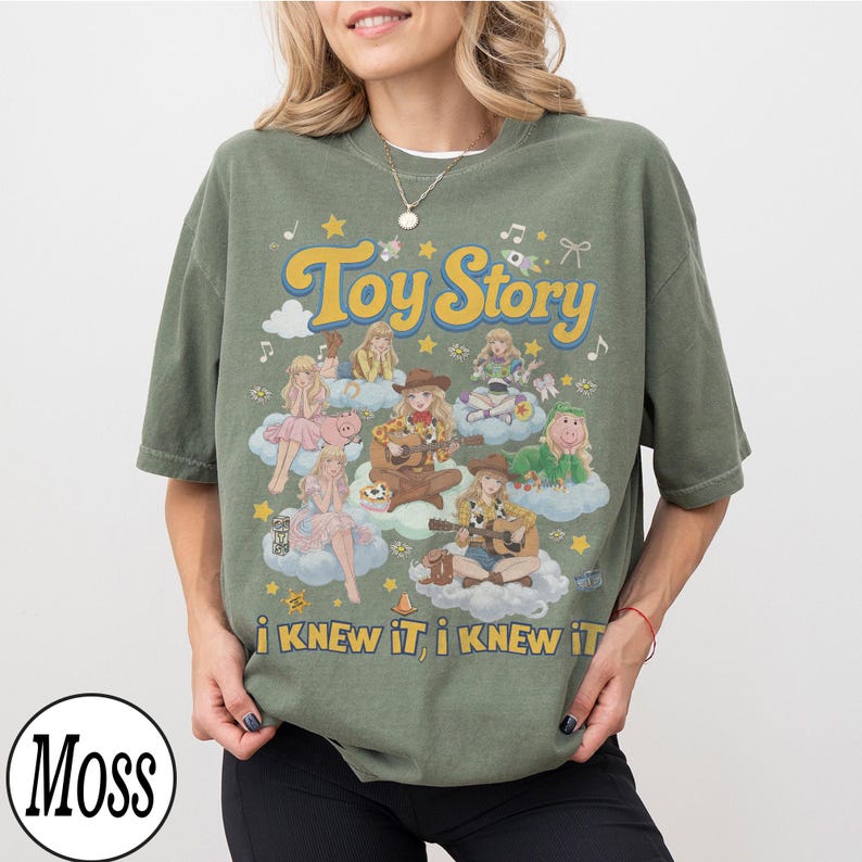 Może przedstawiać: Oliwkowozielony t-shirt z kr&oacute;tkim rękawem z nadrukiem graficznym zawierającym tekst Toy Story oraz i KNEW IT, i KNEW IT. Wz&oacute;r przedstawia wiele postaci w stylu anime siedzących na chmurach, otoczonych gwiazdami, nutami i kokardkami.