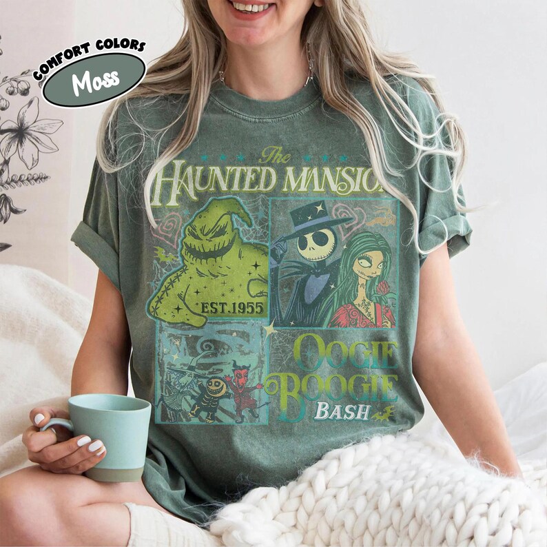 May include: Moss green t-shirt featuring a graphic design with characters from "The Haunted Mansion" and "Oogie Boogie Bash." The design includes the text "The Haunted Mansion," "EST. 1955," and "Oogie Boogie Bash."