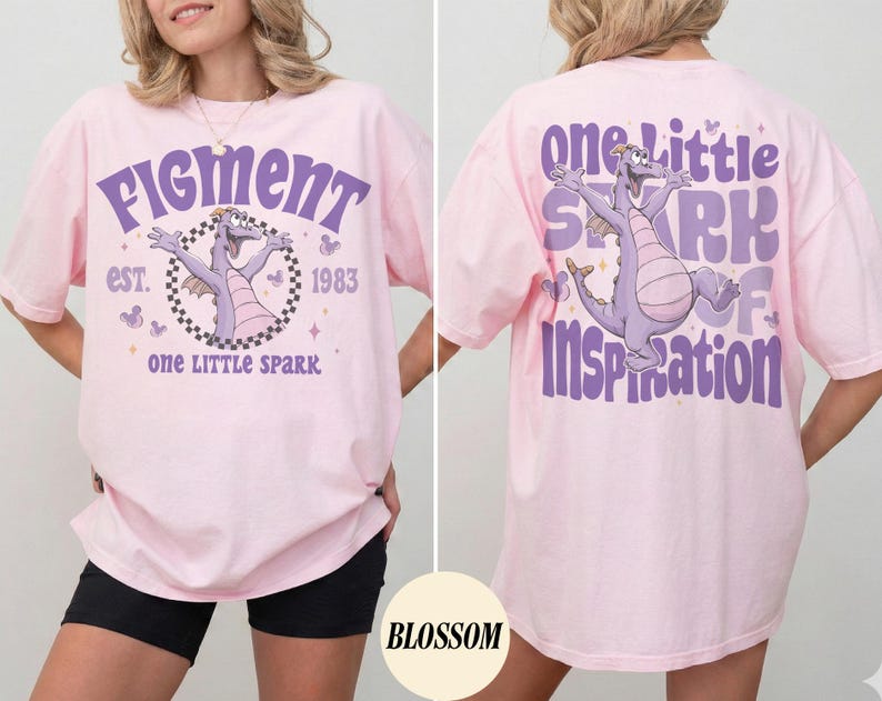 May include: A light pink t-shirt featuring a purple dragon graphic with the text "Figment" and "One Little Spark" on the front. The back of the shirt has the text "One Little Spark of Inspiration" and the same dragon graphic.