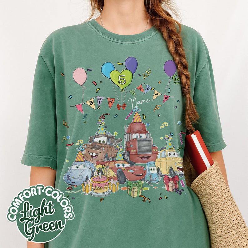 Peut inclure: T-shirt vert clair Comfort Colors avec un motif de voitures de dessins anim&eacute;s c&eacute;l&eacute;brant un anniversaire. Le design comprend des ballons, un g&acirc;teau et le chiffre 5. Les mots "BIRTHDAY" et "Name" sont &eacute;galement visibles.