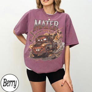 May include: Berry-colored t-shirt featuring a graphic of Mater from the Cars movie. The design includes the word "MATER" above the character, with lightning bolts and tools surrounding the image. The shirt has a relaxed fit.
