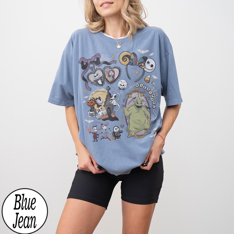 May include: A blue jean t-shirt featuring a colorful graphic of characters from The Nightmare Before Christmas. The design includes Jack Skellington, Sally, Oogie Boogie, and other iconic elements from the movie. The shirt has a round neckline and short sleeves.