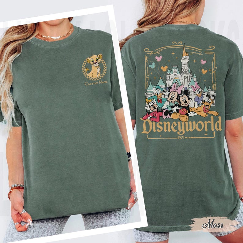 May include: Olive green t-shirt featuring a Simba graphic on the front and a Disneyworld graphic on the back. The Disneyworld graphic includes Mickey Mouse, Minnie Mouse, Donald Duck, Daisy Duck, and Goofy. The shirt has the text "Disneyworld 1971".