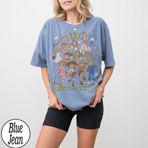 May include: A blue short-sleeve t-shirt featuring a graphic print of various animated characters in different outfits, the letters TS, and the text I KNEW IT. I KNEW YOU. The shirt has a crew neckline and a loose, relaxed fit with a casual appearance.