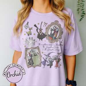 May include: A lilac t-shirt with illustrations of characters from "The Nightmare Before Christmas." The design includes framed portraits of Jack and Sally, Zero, and other characters. The text "The nightmare before Christmas The Dumpkin Queen & The Dumpkin King" is visible.
