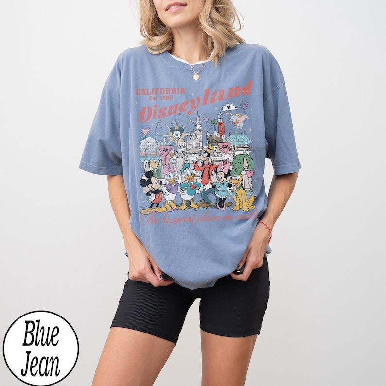 May include: A blue t-shirt with a Disneyland graphic featuring Mickey Mouse, Donald Duck, and other characters. The text "California Disneyland Est. 1955" is printed in red. The shirt has a relaxed fit.