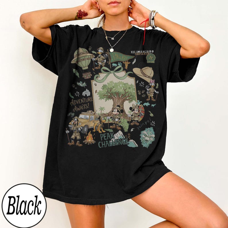 May include: Black t-shirt with a vibrant graphic. The design includes cartoon characters, a tree, and the text "Adventure Awaits!" and "Peak Challenge." The graphic features a jeep, hot air balloon, and safari-themed elements.