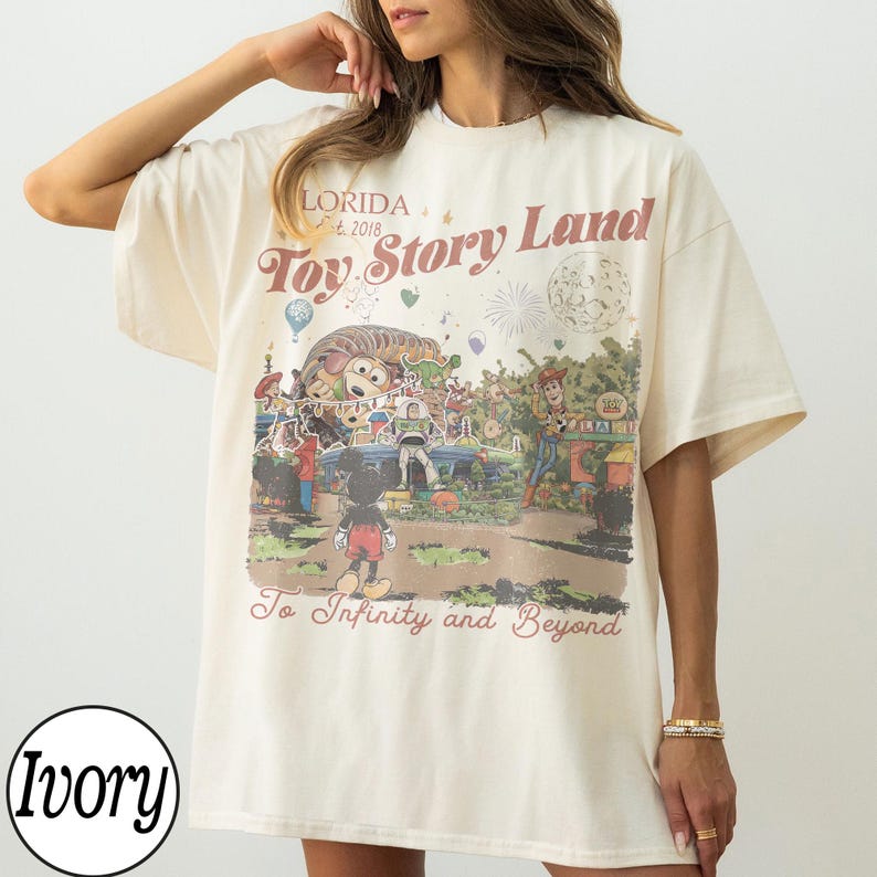 May include: Ivory t-shirt with a vintage Toy Story Land graphic. The design includes Mickey Mouse, Woody, Buzz Lightyear, and the phrase "To Infinity and Beyond." The shirt has short sleeves and a relaxed fit. The text "Florida" is also visible.