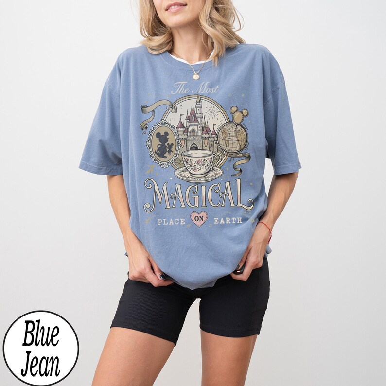 May include: A light blue t-shirt with a graphic that reads "The Most Magical Place on Earth." The graphic includes a castle, teacup, and Mickey Mouse silhouettes. The shirt is a relaxed fit.