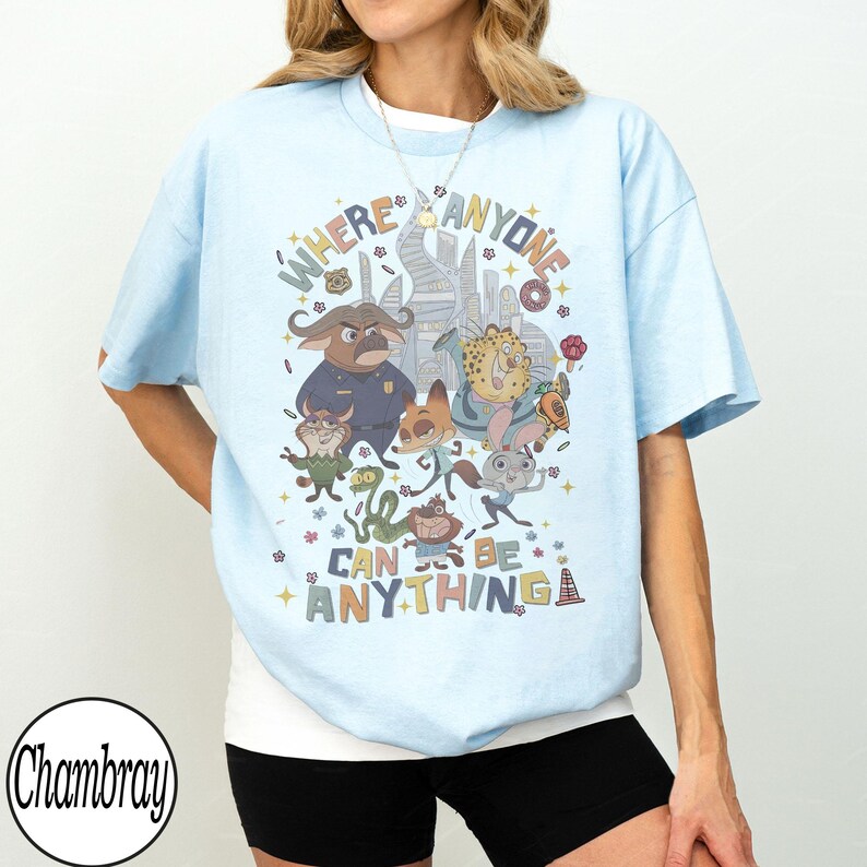 May include: Pale blue t-shirt with a vibrant Zootopia movie graphic. The design showcases characters and the phrase "WHERE ANYONE CAN BE ANYTHING" in a whimsical font. The t-shirt has a loose, comfortable fit.