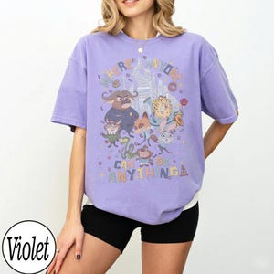 May include: A lilac-coloured t-shirt with a vibrant graphic of cartoon characters and the text "WHERE ANYONE CAN BE ANYTHING". The design includes a cityscape and various animal figures.