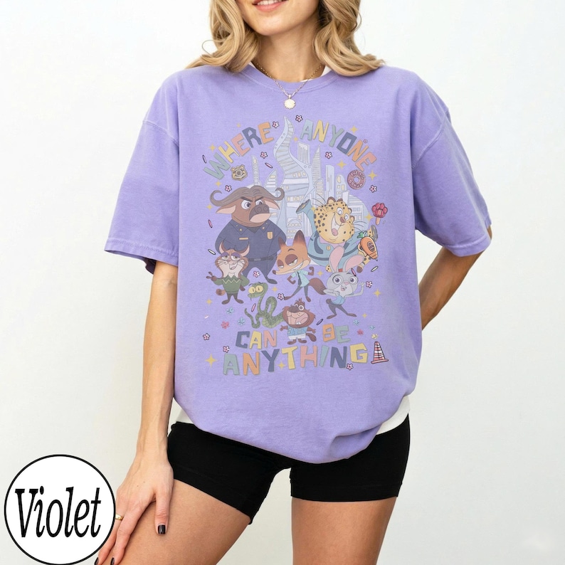 May include: A lilac-coloured t-shirt with a vibrant graphic of cartoon characters and the text "WHERE ANYONE CAN BE ANYTHING". The design includes a cityscape and various animal figures.