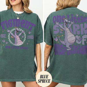 May include: A teal green t-shirt featuring a purple graphic of a cartoon dragon with the text "Figment" and "One Little Spark" on the front. The back of the shirt has a matching graphic and the text "One Little Spark of Imagination".