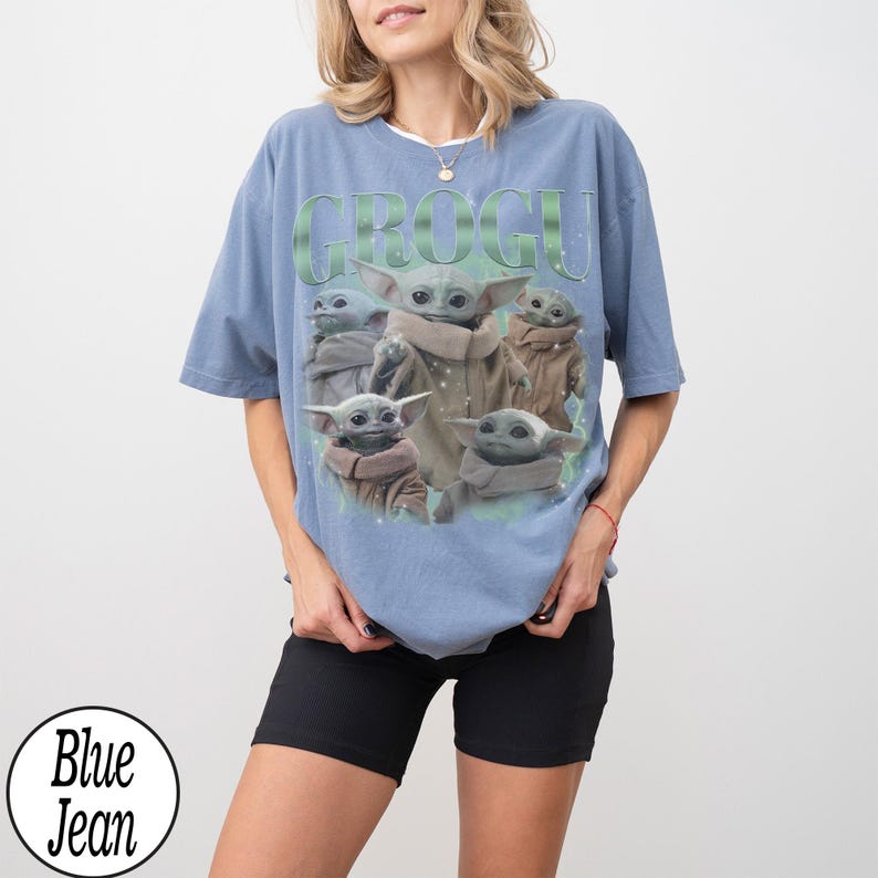 Puede incluir: Una camiseta azul claro con la palabra "GROGU" en letras verdes sobre un gr&aacute;fico de Grogu de The Mandalorian. El gr&aacute;fico muestra a Grogu en varias poses. La camiseta la lleva una persona que lleva pantalones cortos negros.