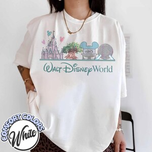 Puede incluir: Camiseta blanca Comfort Colors con un gr&aacute;fico pastel del horizonte de Walt Disney World, que incluye el castillo de Cenicienta, el &Aacute;rbol de la Vida y Spaceship Earth. Las palabras "Walt Disney World" est&aacute;n impresas debajo.