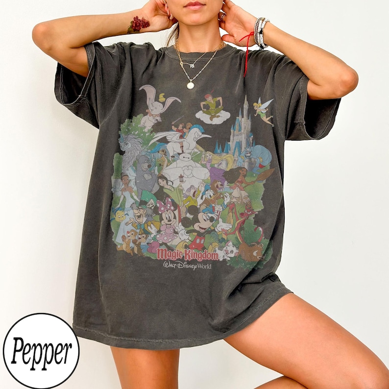 May include: Dark gray t-shirt featuring a colorful graphic of Disney characters, including Mickey Mouse, Minnie Mouse, and Dumbo. The text "Magic Kingdom, Walt Disney World" is printed below the graphic. The shirt has short sleeves and a relaxed fit.