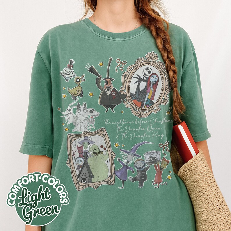 May include: Light green Comfort Colors t-shirt with a design featuring characters from The Nightmare Before Christmas. The design includes framed portraits of Jack and Sally, Oogie Boogie, and other characters. Text on the shirt reads "The Nightmare Before Christmas, The Pumpkin Queen & The Pumpkin King."