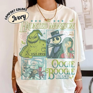 May include: Ivory-colored t-shirt featuring a graphic design with characters from "The Haunted Mansion" and "Oogie Boogie Bash." The design includes the text "The Haunted Mansion" and "EST.1955."