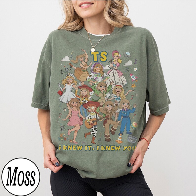 May include: An olive green crew neck t-shirt featuring a graphic print of multiple cartoon characters in various outfits. The text TS is printed at the top, and the text i KNEW IT, i KNEW YOU is printed at the bottom. The design includes musical notes.