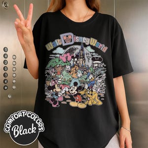 May include: Black Comfort Colors t-shirt featuring a colorful graphic of Disney characters, including Mickey Mouse, Minnie Mouse, Donald Duck, and Goofy, with the text "Walt Disney World".