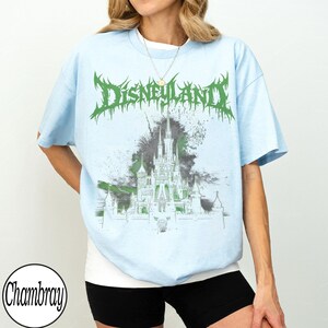 May include: Light blue t-shirt with a green and gray graphic of a castle and the word "Disneyland" in a spiky font. The shirt has short sleeves and a crew neck.