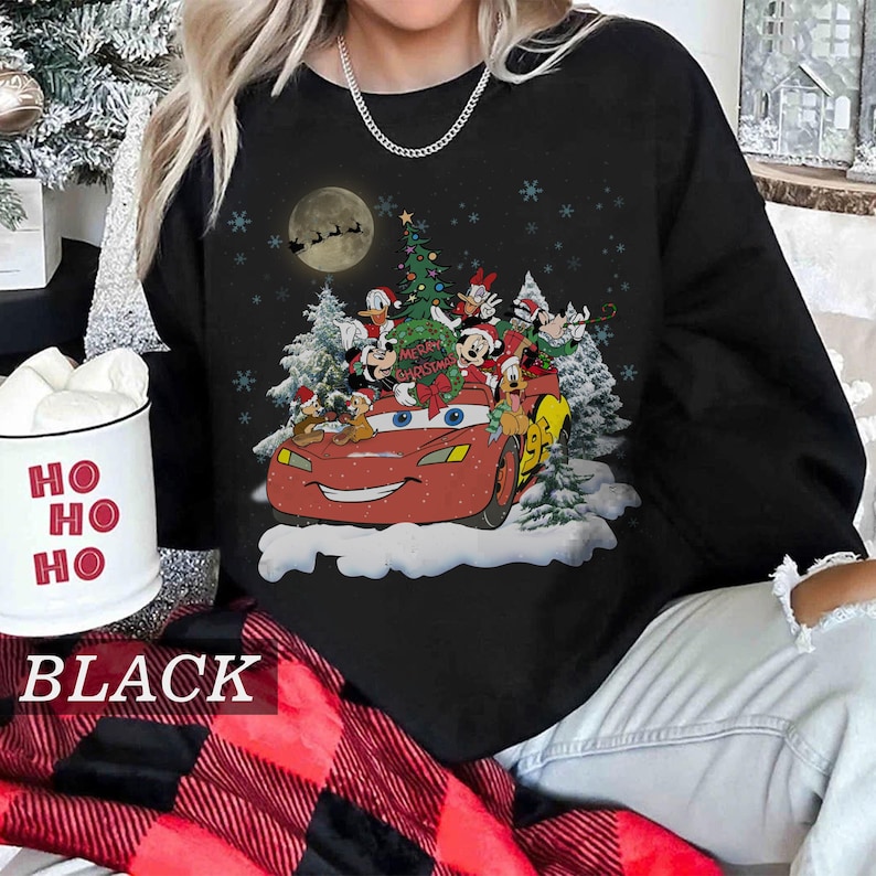 K&ouml;nnte beinhalten: Schwarzes Sweatshirt mit Rundhalsausschnitt und einem weihnachtlichen Motiv. Das Design zeigt Lightning McQueen aus dem Film Cars, umgeben von Disney-Figuren, einem Weihnachtsbaum und Schneeflocken. Der Text "Merry Christmas" ist ebenfalls enthalten.