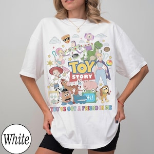 May include: A white t-shirt featuring a colorful graphic print of various Toy Story characters including Buzz Lightyear, Woody, Jessie, and Mr. Potato Head. The text TOY STORY and YOU'VE GOT A FRIEND IN ME are printed in the center of the design.