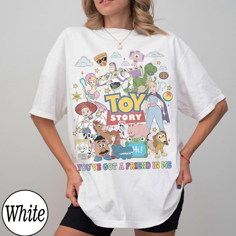 May include: A white t-shirt featuring a colorful graphic print of various Toy Story characters including Buzz Lightyear, Woody, Jessie, and Mr. Potato Head. The text TOY STORY and YOU'VE GOT A FRIEND IN ME are printed in the center of the design.