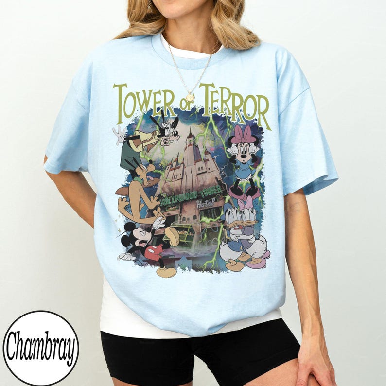 K&ouml;nnte beinhalten: Hellblaues T-Shirt mit einer Grafik des Hollywood Tower Hotels, Mickey Mouse, Minnie Mouse, Donald Duck und Goofy. Der Text "Tower of Terror" ist in Gr&uuml;n &uuml;ber der Grafik aufgedruckt.