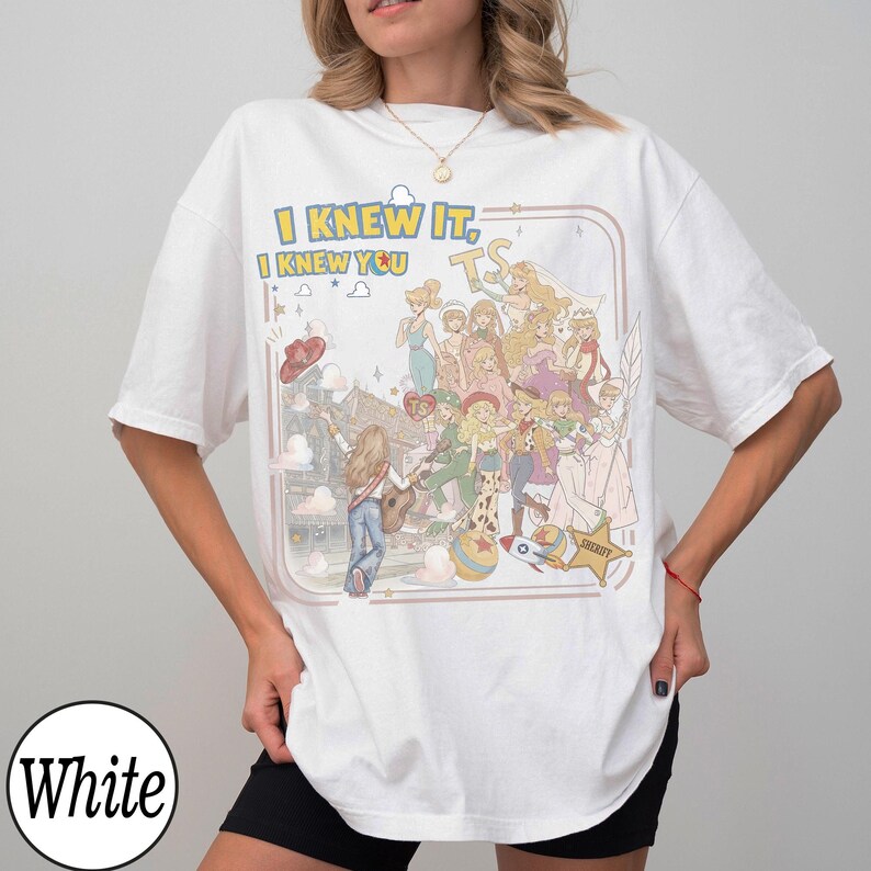 May include: A white short-sleeved t-shirt featuring a colorful graphic print with the text "I KNEW IT, I KNEW YOU". The illustration depicts a collage of various animated characters in different outfits, a guitar, a rocket, and a sheriff star badge.