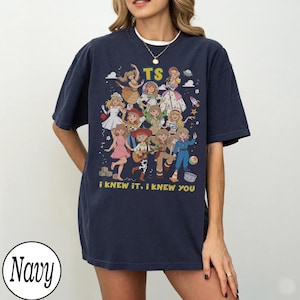 May include: A navy blue short-sleeve t-shirt featuring a graphic print of multiple cartoon characters in various outfits. The text "TS" appears at the top, and the text "i KNEW IT, i KNEW YOU" is printed in yellow at the bottom of the graphic.