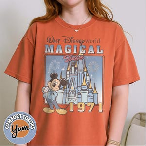 May include: Burnt orange t-shirt featuring a graphic of Mickey Mouse in front of Cinderella's castle. The shirt has the text "Walt Disney World MAGICAL Since 1971". The shirt is from Comfort Colors.
