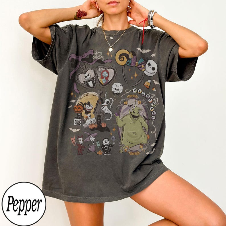 May include: Dark gray t-shirt featuring a colorful graphic design with characters and elements from "The Nightmare Before Christmas." The design includes Jack Skellington, Sally, Oogie Boogie, and other iconic imagery. The shirt has short sleeves and a relaxed fit.