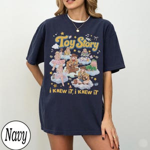 Może przedstawiać: Granatowa koszulka z kr&oacute;tkim rękawem z nadrukiem graficznym zawierającym tekst "Toy Story" oraz "i KNEW iT, i KNEW iT". Wz&oacute;r przedstawia wiele ilustrowanych postaci siedzących na chmurach, otoczonych gwiazdami, nutami i drobnymi symbolami.