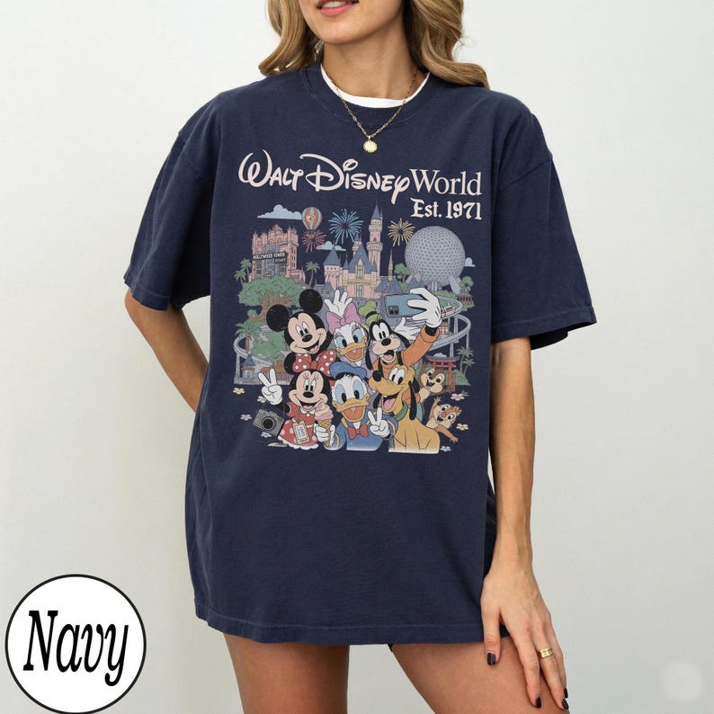 May include: A navy blue short-sleeve t-shirt featuring a graphic print of Walt Disney World Est. 1971 with various cartoon characters including Mickey Mouse, Minnie Mouse, Donald Duck, Daisy Duck, Goofy, Pluto, and Chip 'n Dale in front of park landmarks.
