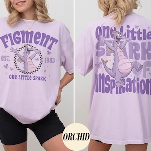May include: A light purple t-shirt featuring a cartoon dragon with the text "Figment" and "one LITTLE spark" on the front. The back of the shirt has the text "one little spark of inspiration" and a matching dragon graphic.