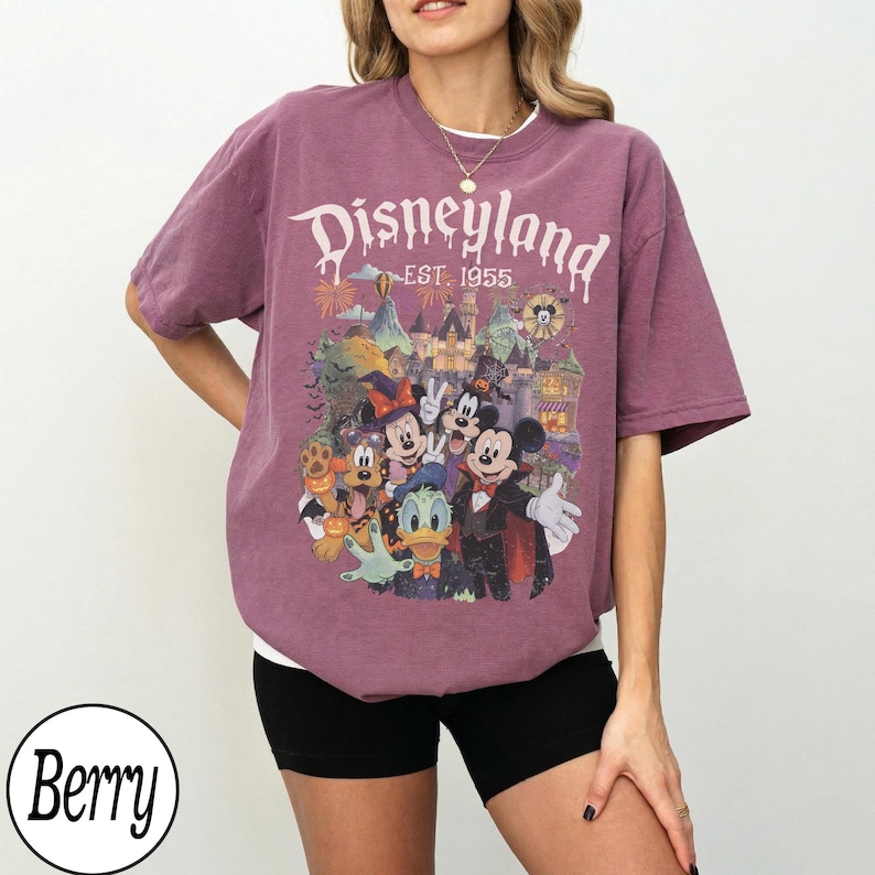 Puede incluir: Una camiseta de manga corta color baya con un estampado gr&aacute;fico de personajes de Disney con disfraces de Halloween frente a un castillo. El texto dice Disneyland EST. 1955. El dise&ntilde;o incluye a Mickey Mouse, Minnie Mouse, Donald Duck y Pluto.