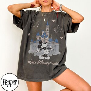 May include: Dark grey t-shirt with a graphic of Mickey Mouse in front of a castle, fireworks, and the text "Walt Disney World." The shirt has short sleeves and a relaxed fit.