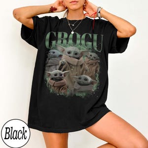 Puede incluir: Camiseta negra con un gr&aacute;fico de Grogu, tambi&eacute;n conocido como Baby Yoda, rodeado de una niebla verde. La palabra "GROGU" est&aacute; impresa en verde encima de la imagen. La camiseta es de corte holgado.