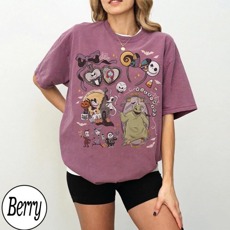 May include: Berry-colored t-shirt featuring a colorful graphic print of characters from The Nightmare Before Christmas. The design includes Jack Skellington, Sally, Oogie Boogie, and other Halloween-themed elements. The shirt has short sleeves and a crew neck.