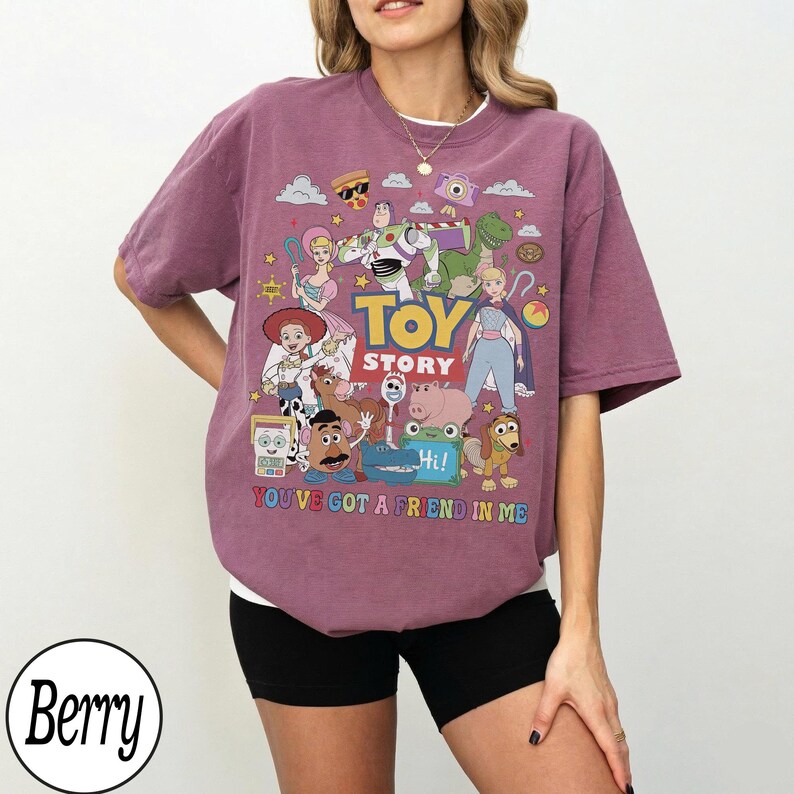 May include: A berry-colored t-shirt featuring a graphic print of Toy Story characters including Woody, Buzz Lightyear, and Jessie. The text reads TOY STORY and YOU'VE GOT A FRIEND IN ME. The design includes various colorful icons and movie figures.