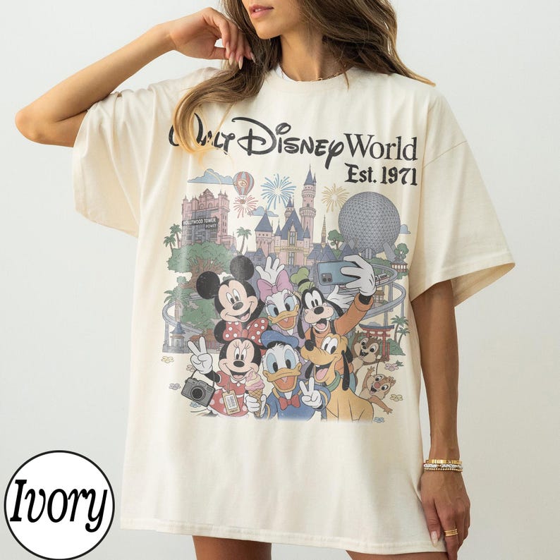 May include: An ivory short-sleeve t-shirt featuring a graphic print of Walt Disney World Est. 1971. The design includes Mickey Mouse, Minnie Mouse, Donald Duck, Daisy Duck, Goofy, Pluto, and Chip 'n Dale in front of park landmarks.