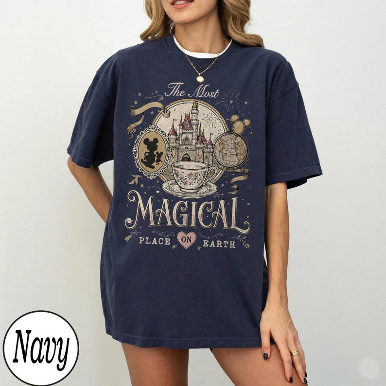 May include: Navy blue t-shirt with a graphic design featuring a castle, teacup, and Mickey Mouse. The text reads "The Most Magical Place on Earth." The design is in shades of beige, brown, and white.