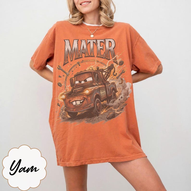 May include: Orange t-shirt featuring a graphic of Mater from the movie Cars. The design includes the word "MATER" in a distressed font above the character. The shirt has short sleeves and a relaxed fit, suitable for casual wear.