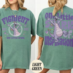 May include: Light green t-shirt featuring a purple dragon graphic with the text "Figment" and "One Little Spark" on the front. The back of the shirt has a matching dragon graphic and the words "One Little Spark of Inspiration".