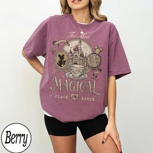 May include: Berry-colored t-shirt with a graphic design featuring a castle, teacup, and Mickey Mouse. The text on the shirt reads "The Most Magical Place on Earth."
